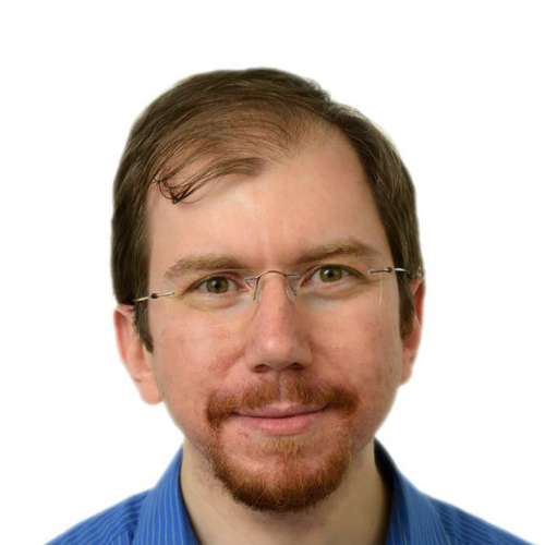 man with glasses and dark hair smiling. he is wearing a blue shirt